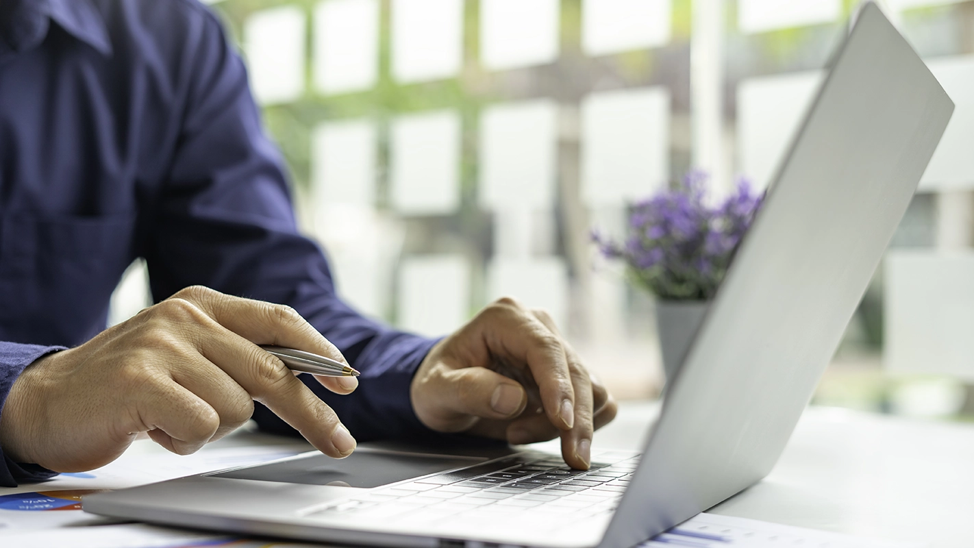 An illustrative adult using a laptop with a notebook and pen
